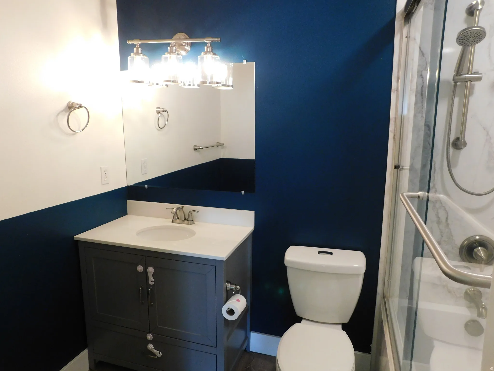 Modern bathroom featuring a navy and white color scheme with a dark vanity cabinet, white rectangular sink, polished chrome faucet, and integrated lighting above the mirror
