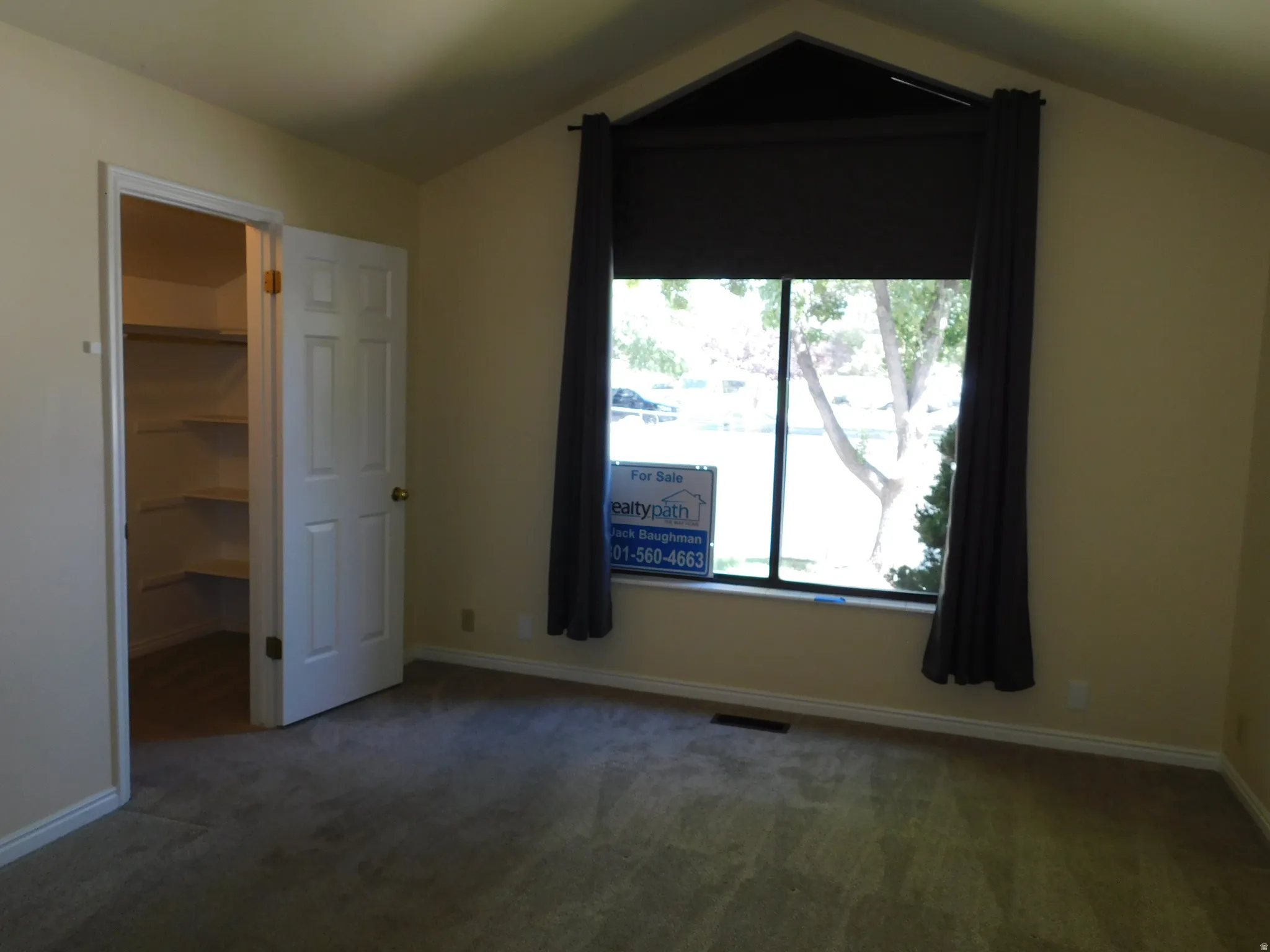 Vaulted ceiling with an architectural window feature, soft carpet flooring, and a closet with built-in shelving