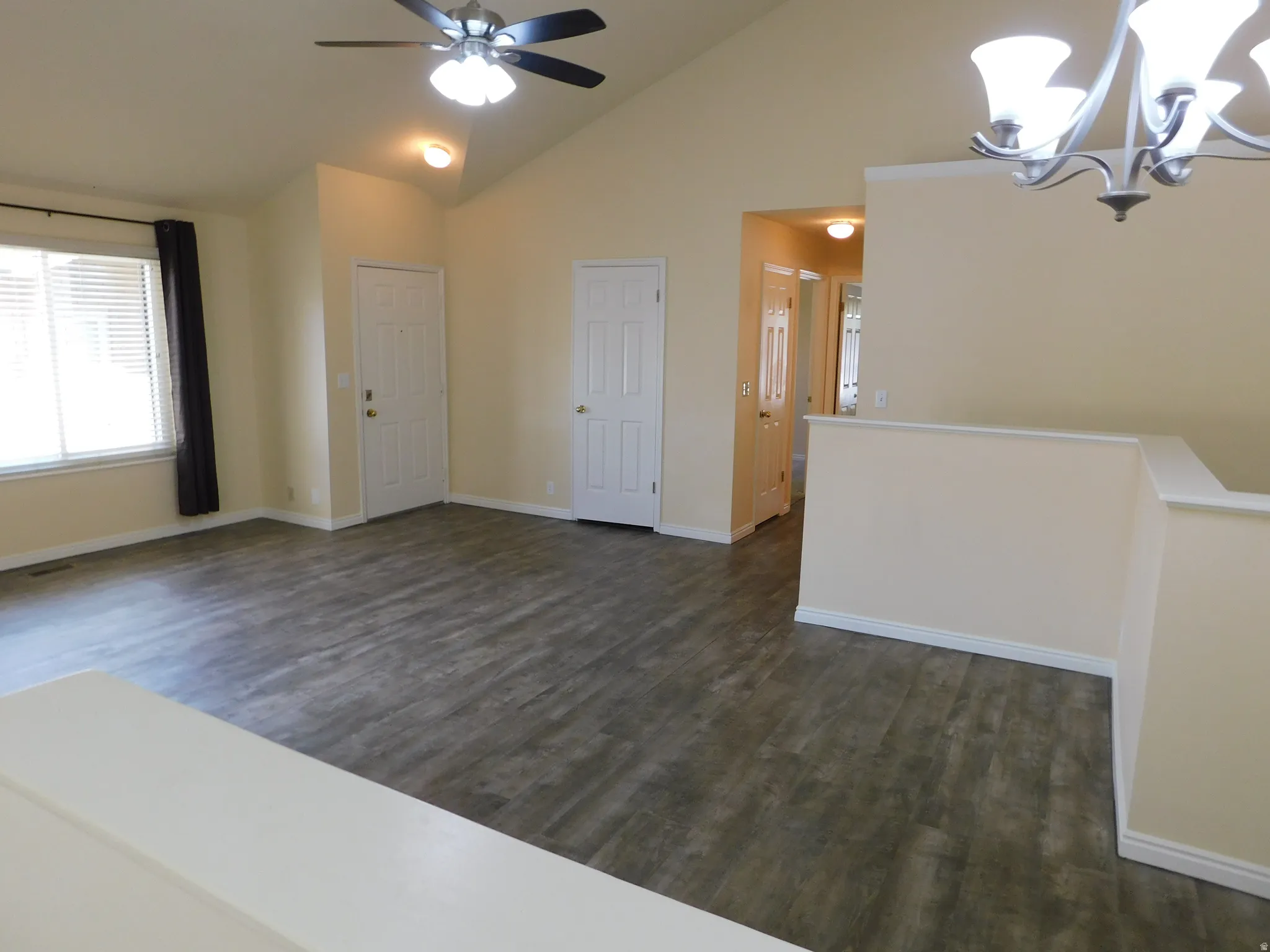 Vaulted ceiling with an attached ceiling fan, wood-finish flooring, and white interior doors
