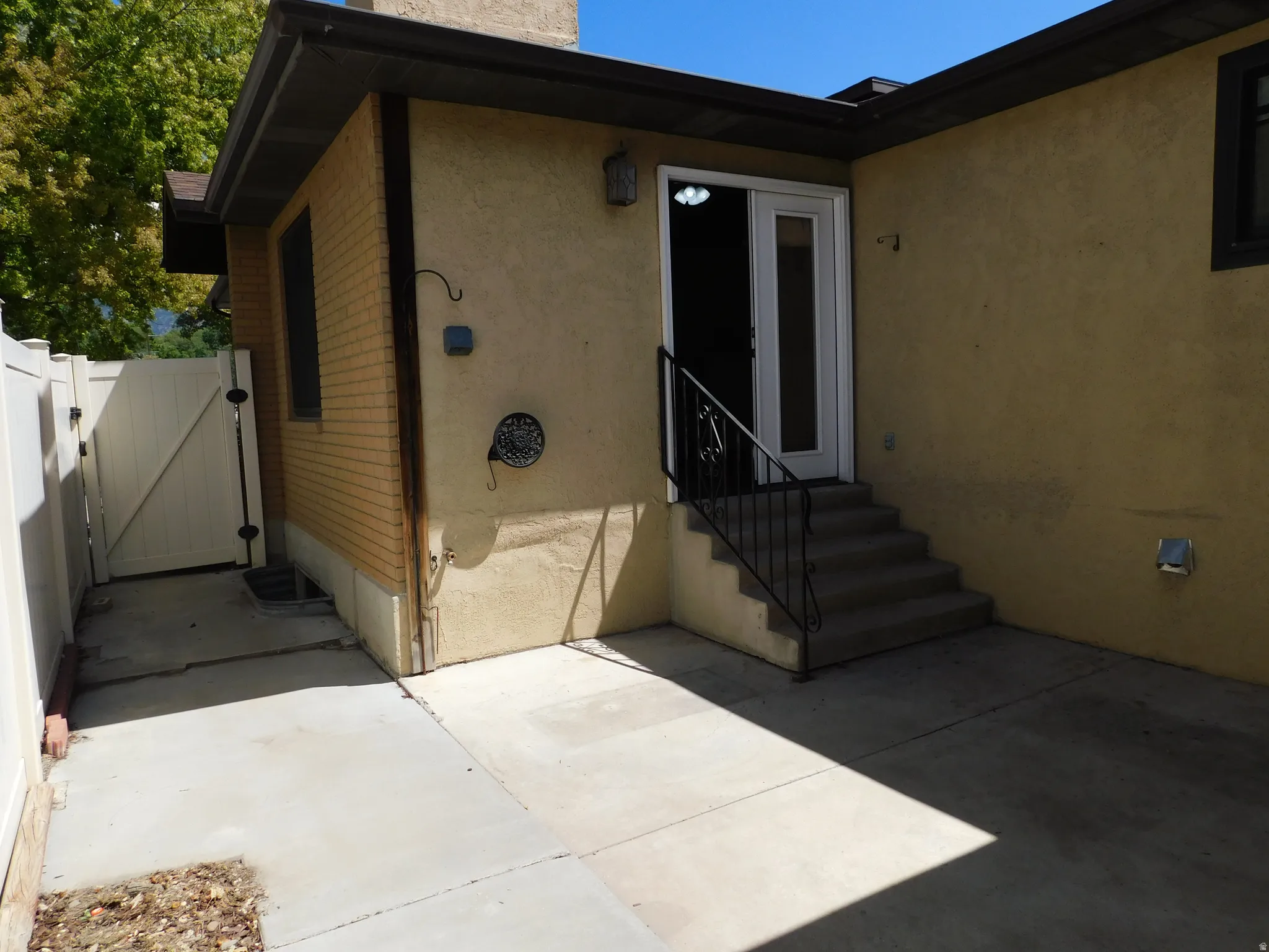Stucco exterior with a security door, concrete patio, and a white privacy fence
