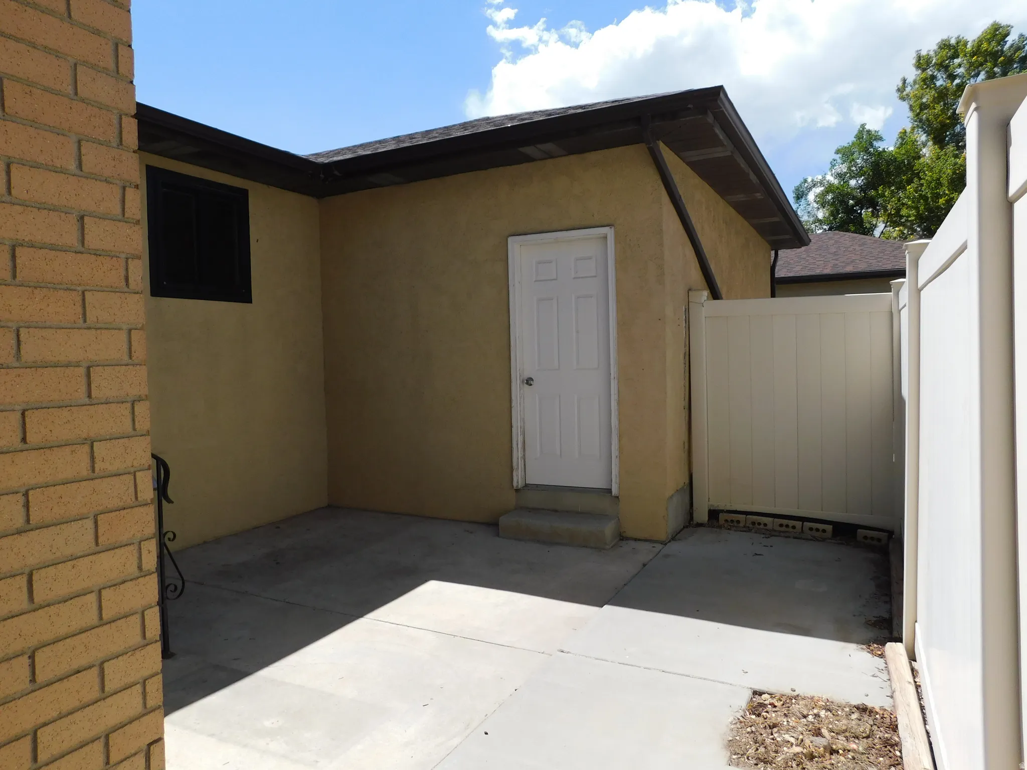 Exterior featuring stucco siding, brick detailing, a white privacy fence, and a concrete patio