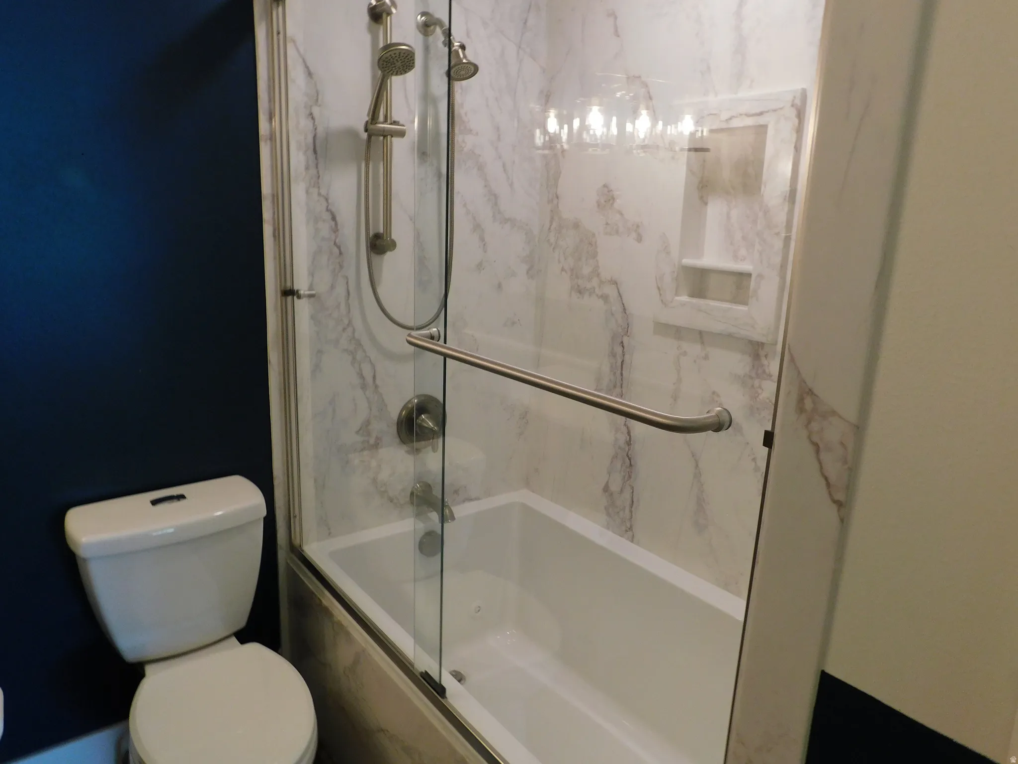 Bathtub with a glass shower enclosure, a built-in shower niche, and a showerhead with a handheld sprayer