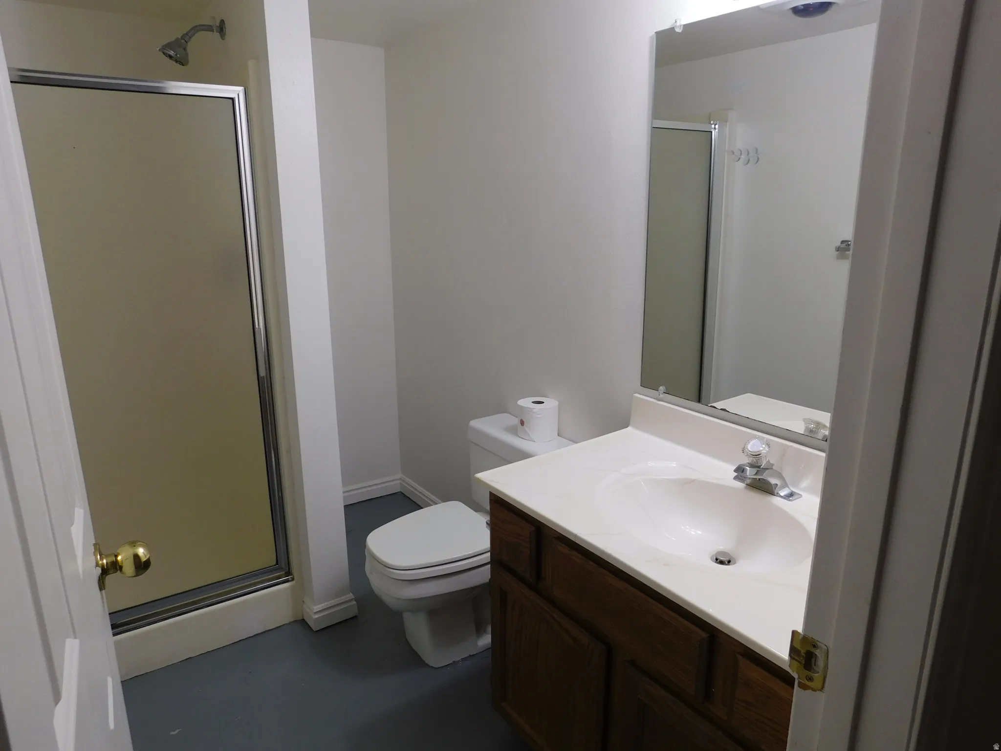 Bathroom featuring a shower with a sliding glass door, a vanity with a white countertop and integrated sink, a wood-finish cabinet, and a wall-mounted mirror