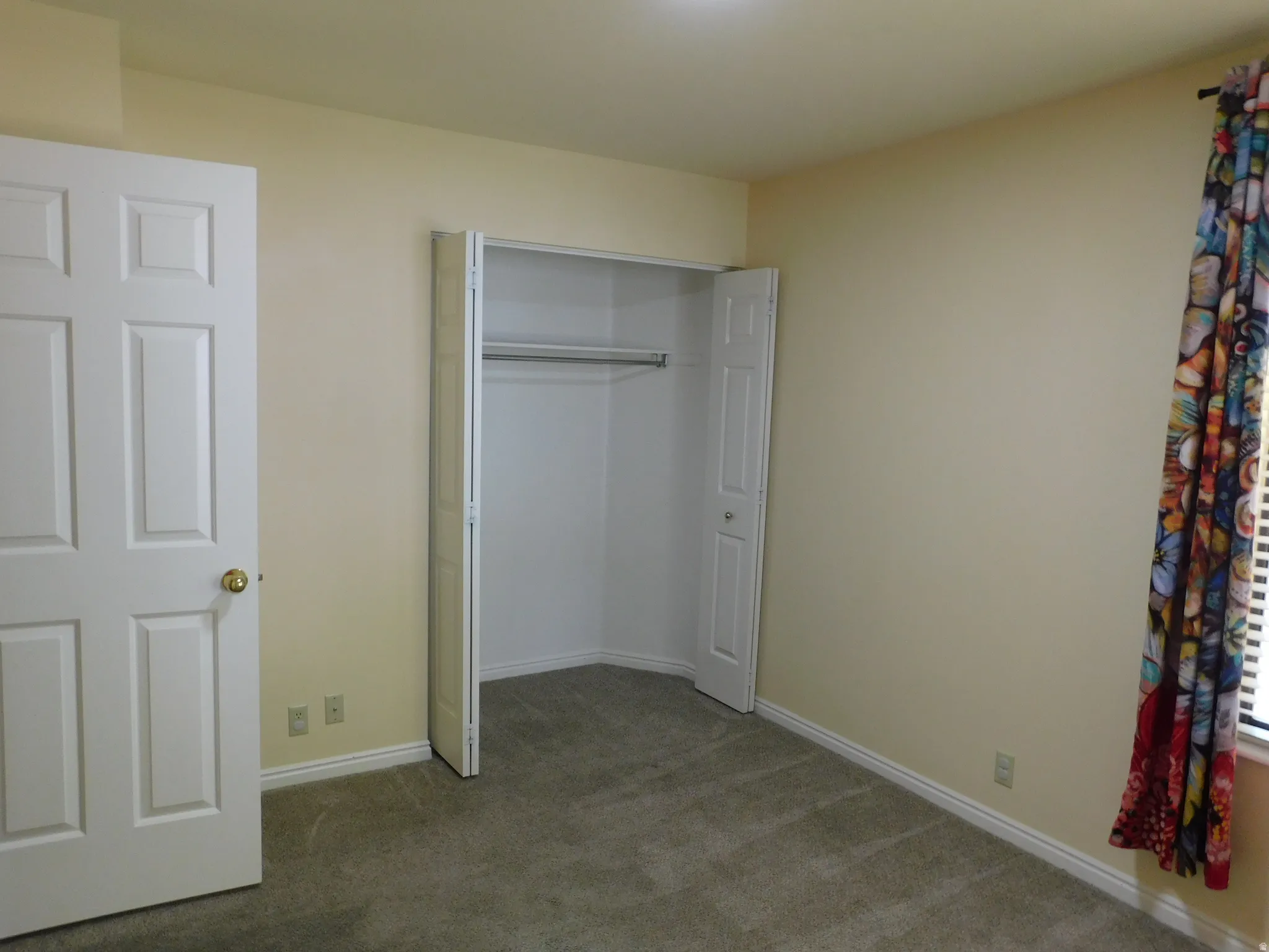 Neutral-toned carpeting, light-colored walls, and a built-in closet with bi-fold doors