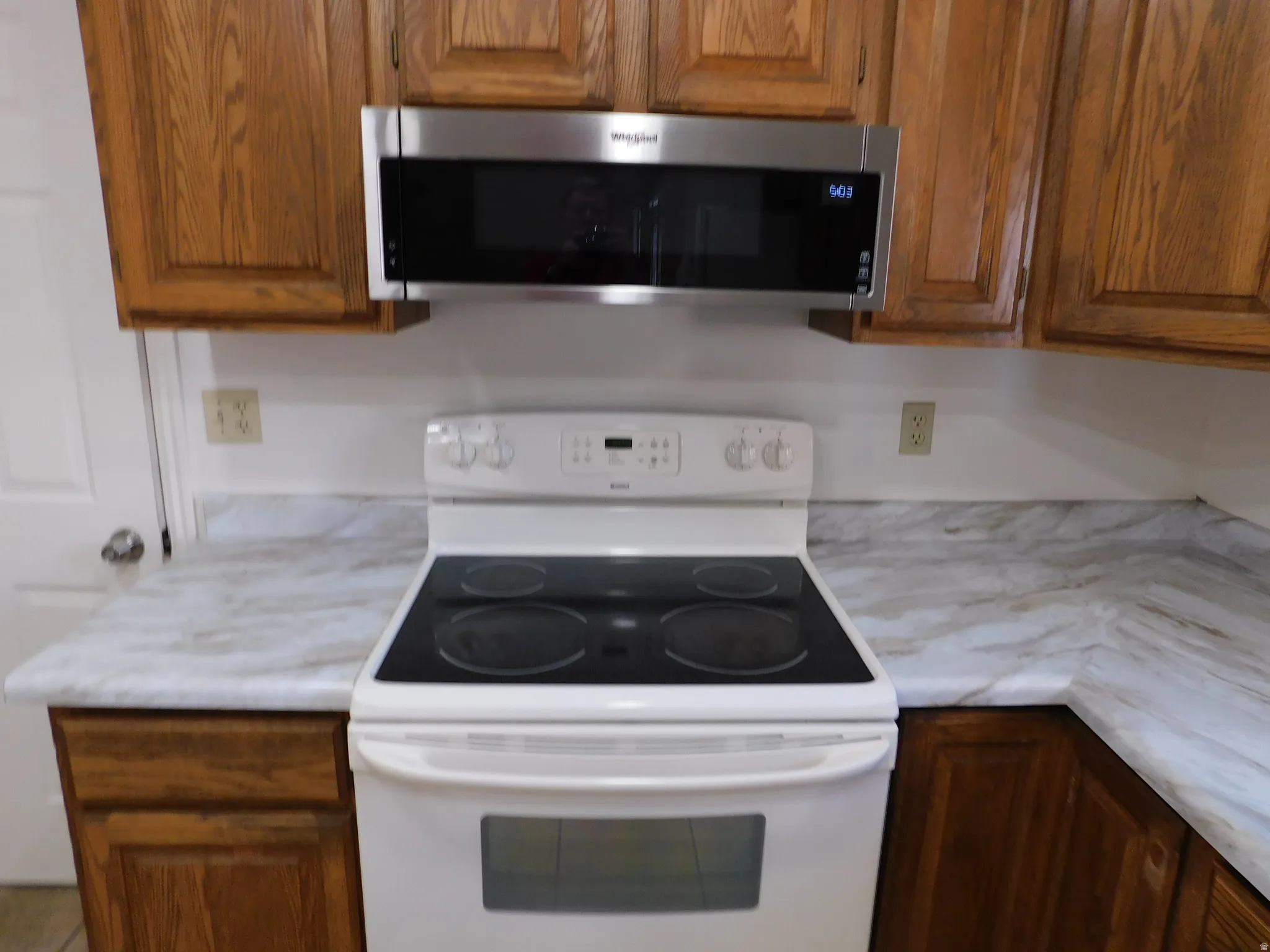 Oak wood-finish cabinetry with a stainless steel microwave oven and white electric range