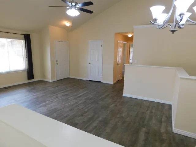 Vaulted ceiling with an attached ceiling fan, wood-finish flooring, and white interior doors