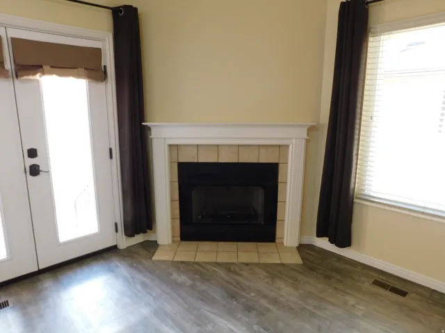 Fireplace with tile surround and white mantel, wood-finish flooring, and French doors with privacy shades