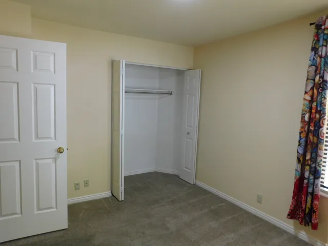 Neutral-toned carpeting, light-colored walls, and a built-in closet with bi-fold doors