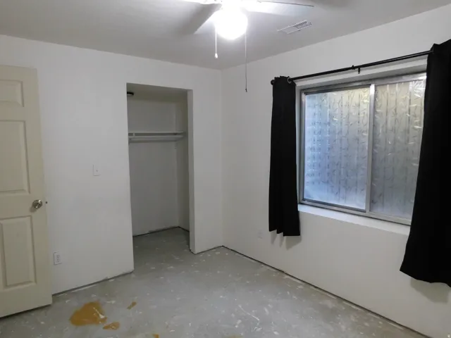 Recessed closet with a single hanging rod, ceiling fan with illumination, and a window