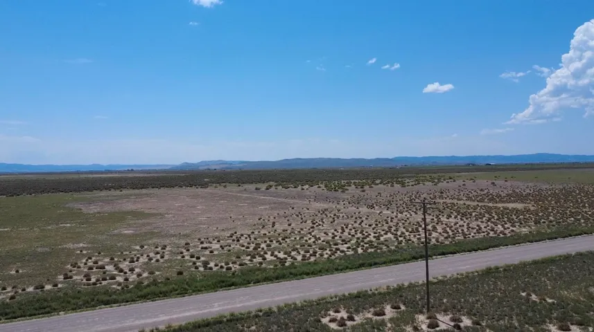 Expansive rural landscape featuring a dirt road, utility pole, and distant mountain ranges under a clear sky