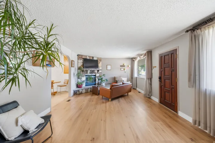 Spacious living area featuring wood-finish flooring, a stone-clad fireplace, and a paneled entry door
