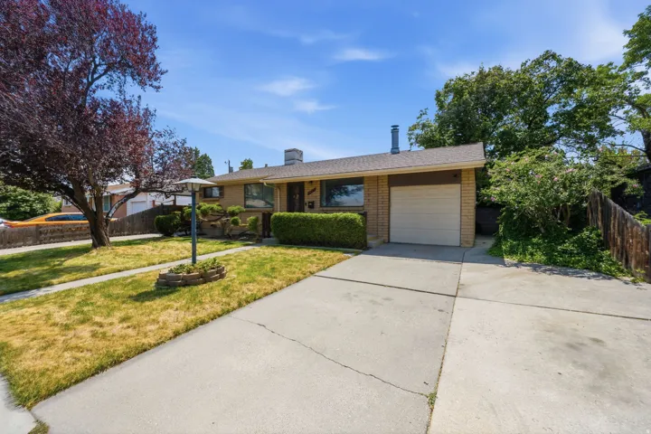 Brick exterior, attached garage, paved driveway, mature landscaping, and front yard