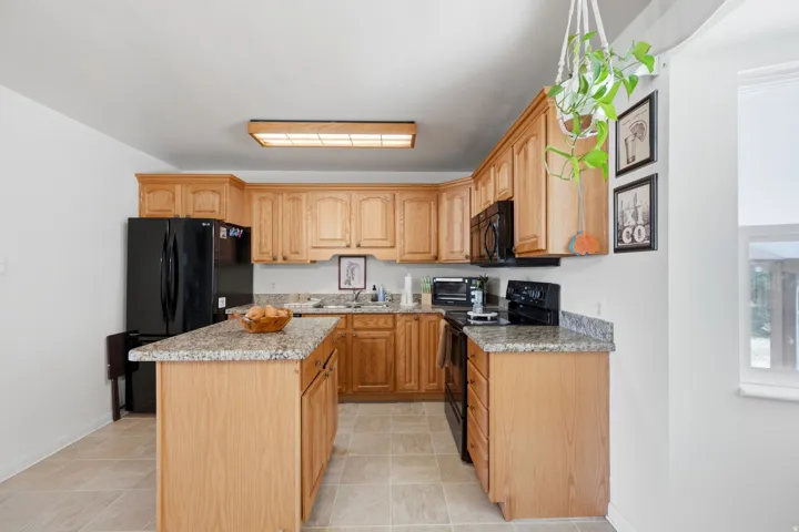Kitchen featuring wood-finish cabinetry, black appliances, granite countertops, and a center island