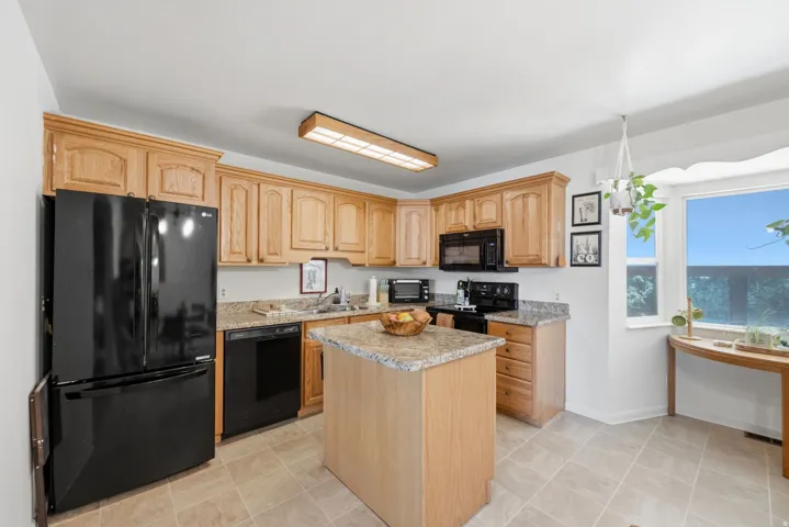 Wood-finish cabinetry, granite-style countertops, stainless steel sink, black appliances, and tiled flooring