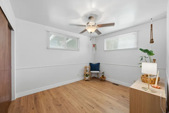 Wood-finish flooring, white walls with wainscoting, two horizontal windows, and a ceiling fan with integrated lighting