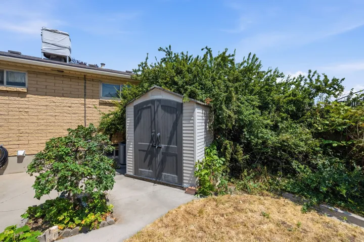 Detached storage shed with double doors, paved pathway, and established perimeter foliage