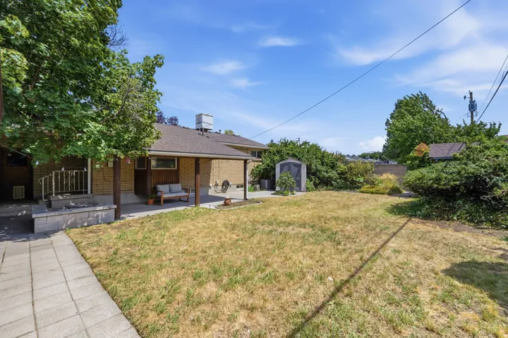 Expansive backyard featuring a covered patio, a detached shed, and mature perimeter landscaping