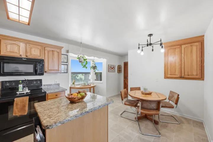 Kitchen featuring wood cabinetry, granite countertops, black appliances, and tile flooring