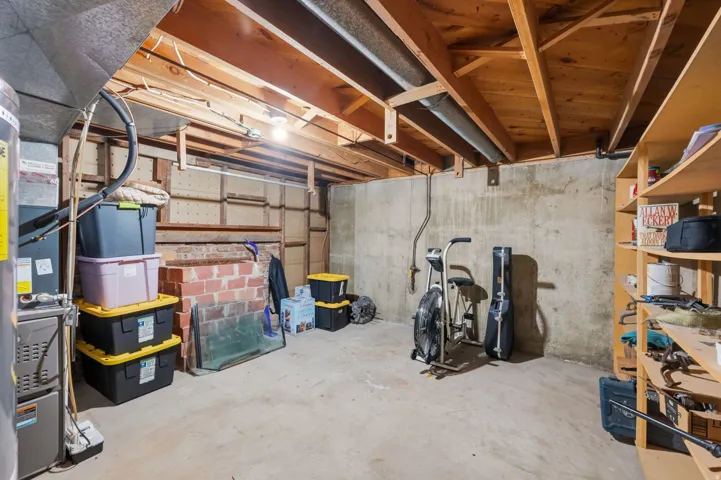Concrete flooring, exposed ceiling joists, concrete foundation walls, built-in wooden shelving, and a brick-built feature