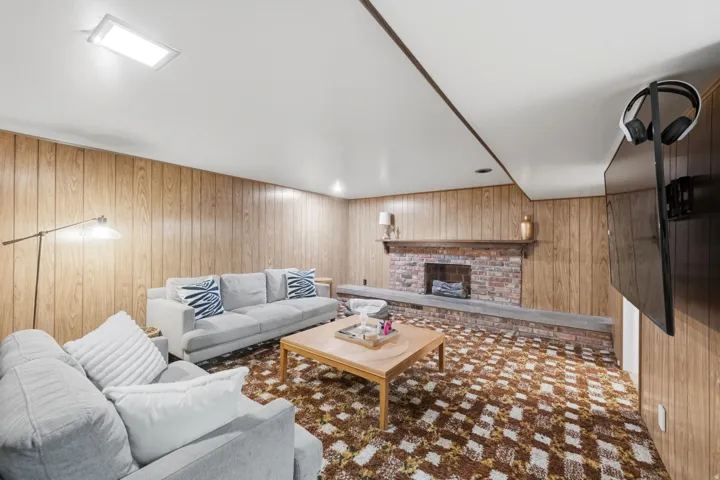 Wood paneling walls, a brick fireplace with a stone hearth, a ceiling-mounted rectangular light fixture, and a wall-mounted display