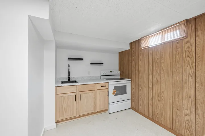 Kitchenette featuring light wood-finish cabinetry, a black sink with a tall faucet, a white range, and a light-toned countertop