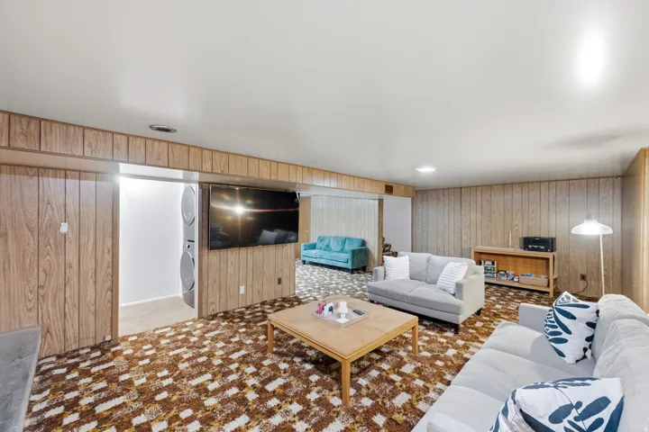 Expansive room featuring wood-finish wall paneling, a patterned carpet, and built-in stacked laundry appliances