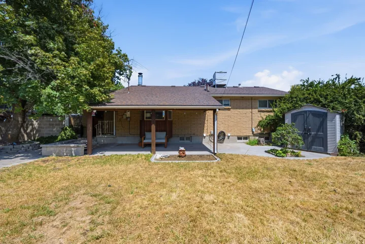 Expansive backyard featuring a covered patio, concrete hardscaping, a storage shed, and mature perimeter trees