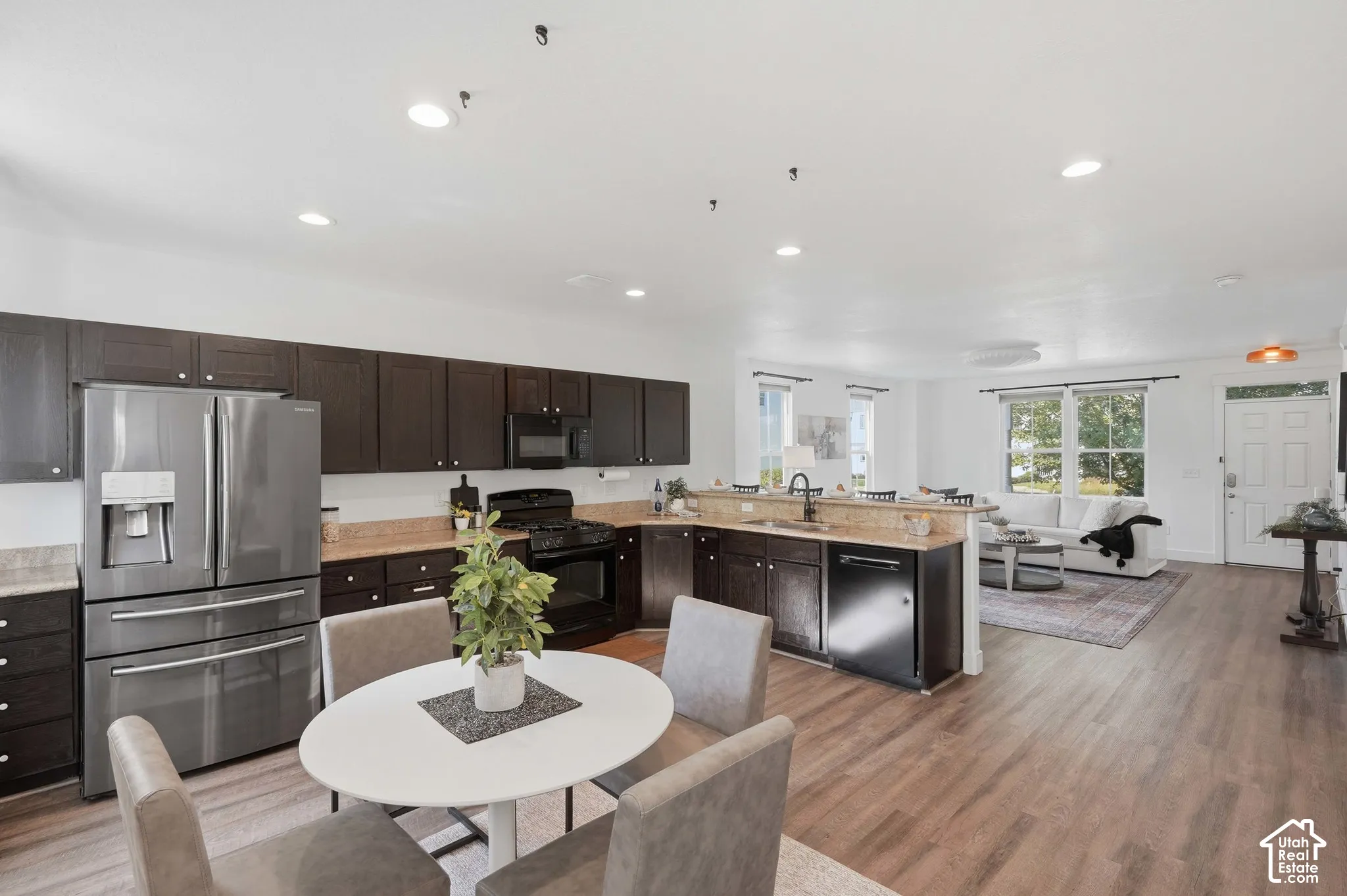 Open-concept living space with wood-finish flooring, recessed lighting, and a kitchen featuring dark cabinetry, stainless steel appliances, and light-toned countertops
