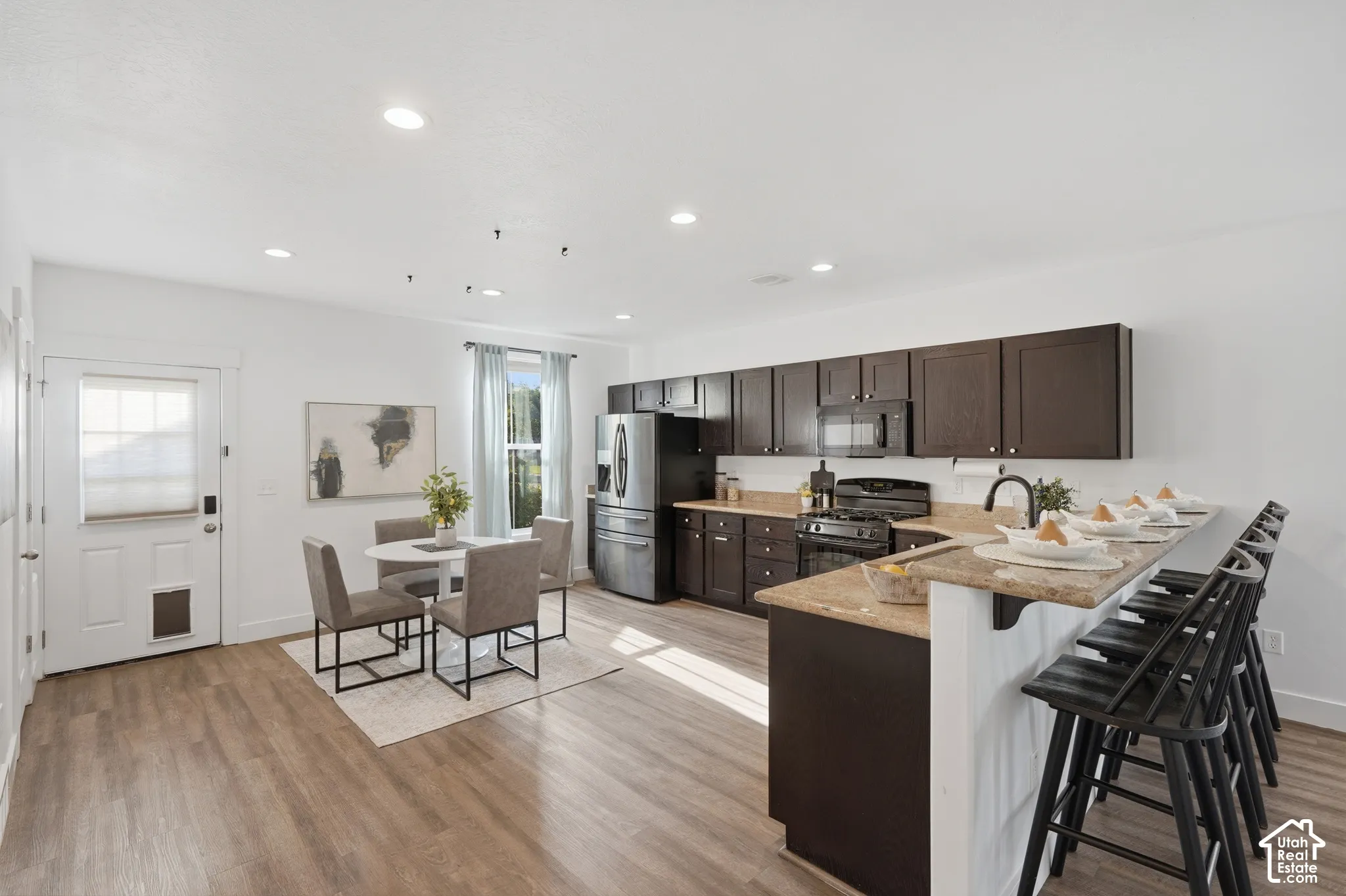 Open-concept kitchen featuring dark wood cabinetry, light-colored countertops, stainless steel appliances, and wood-finish flooring