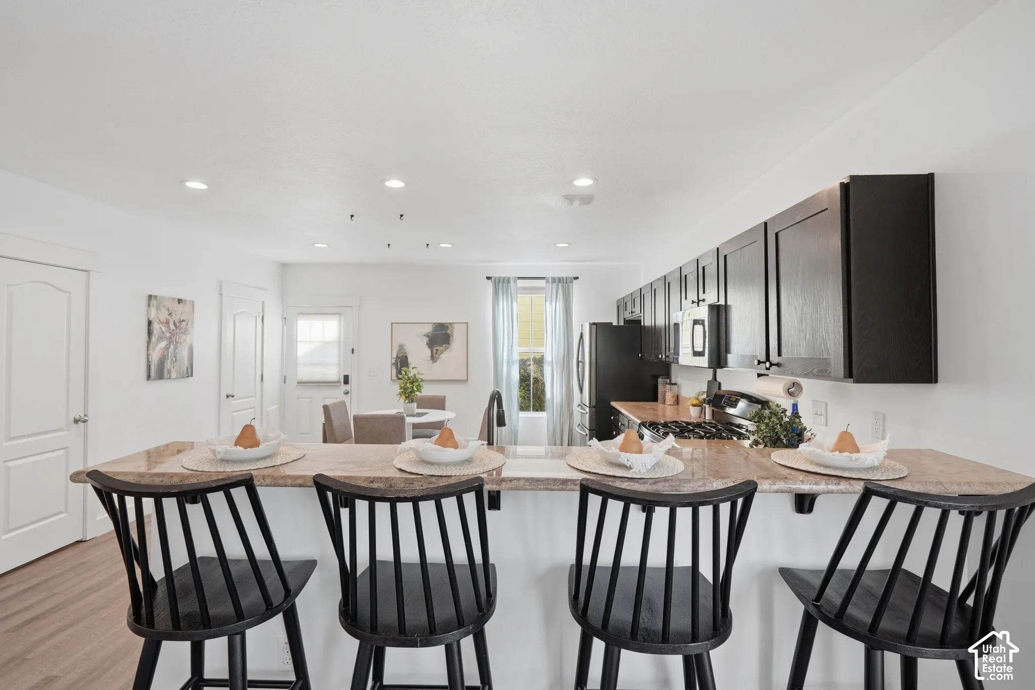Kitchen featuring an eat-at island with a stone-finish countertop, black cabinetry, recessed lighting, and wood-finish flooring