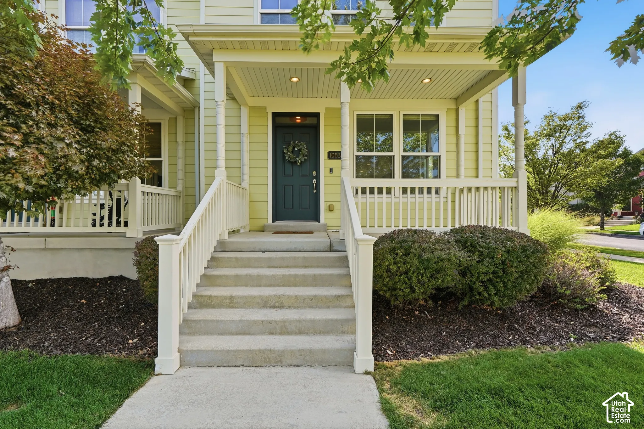 Covered front porch with a paneled front door, white railing, and exterior lighting