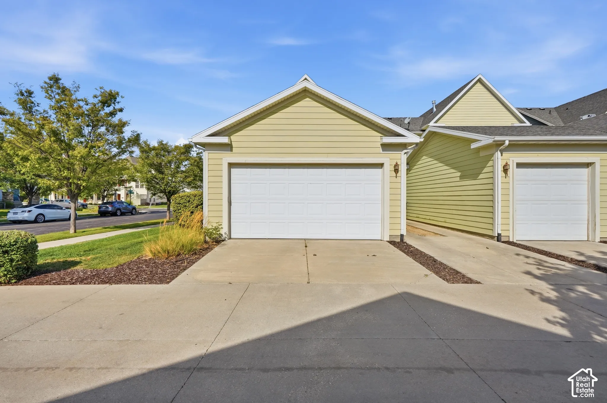 Light-toned siding exterior with two garage doors, concrete driveways, and integrated exterior lighting fixtures