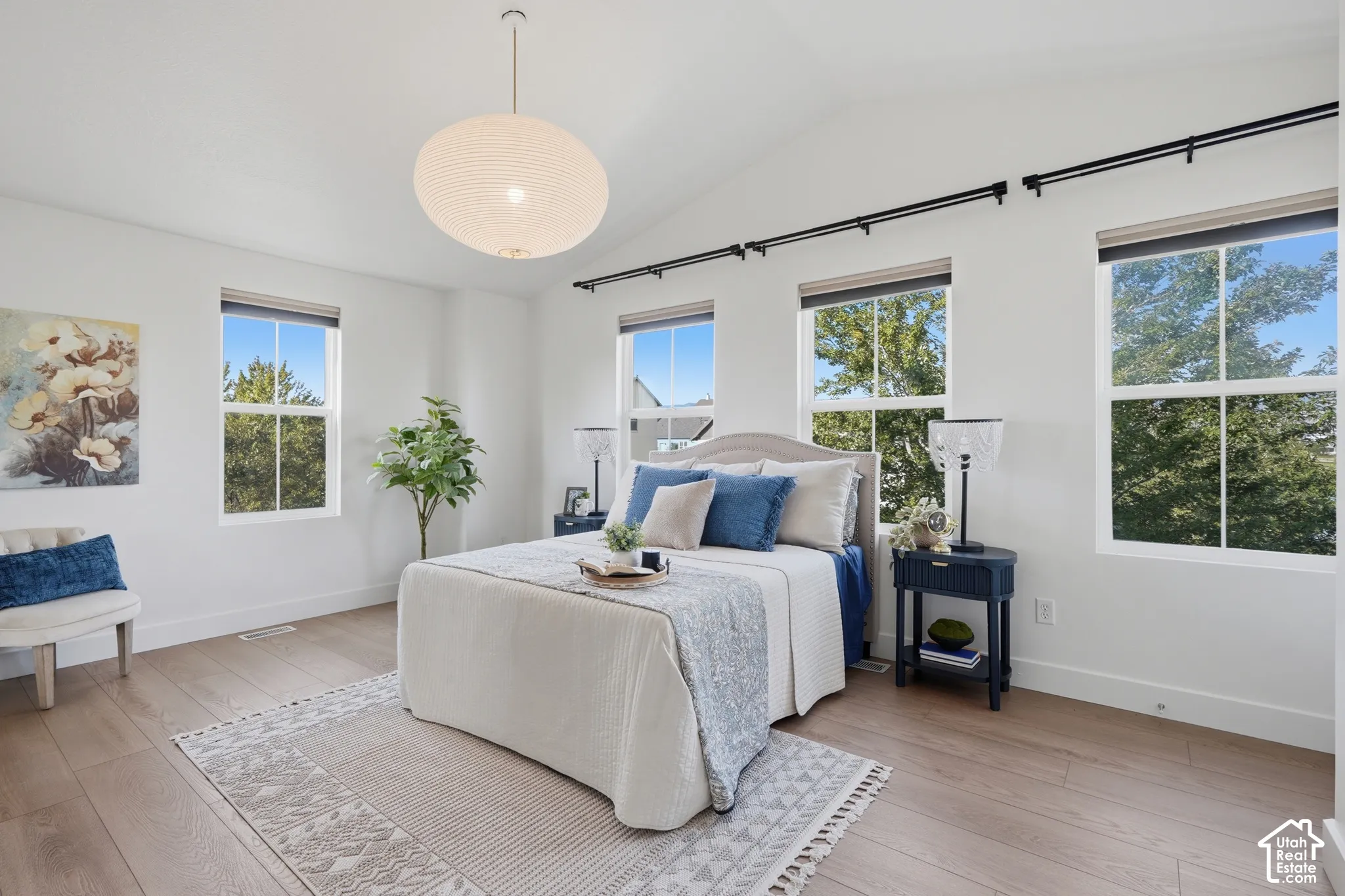 Vaulted ceiling with a suspended lighting fixture, multiple double-hung windows, wood-finish flooring, and white walls
