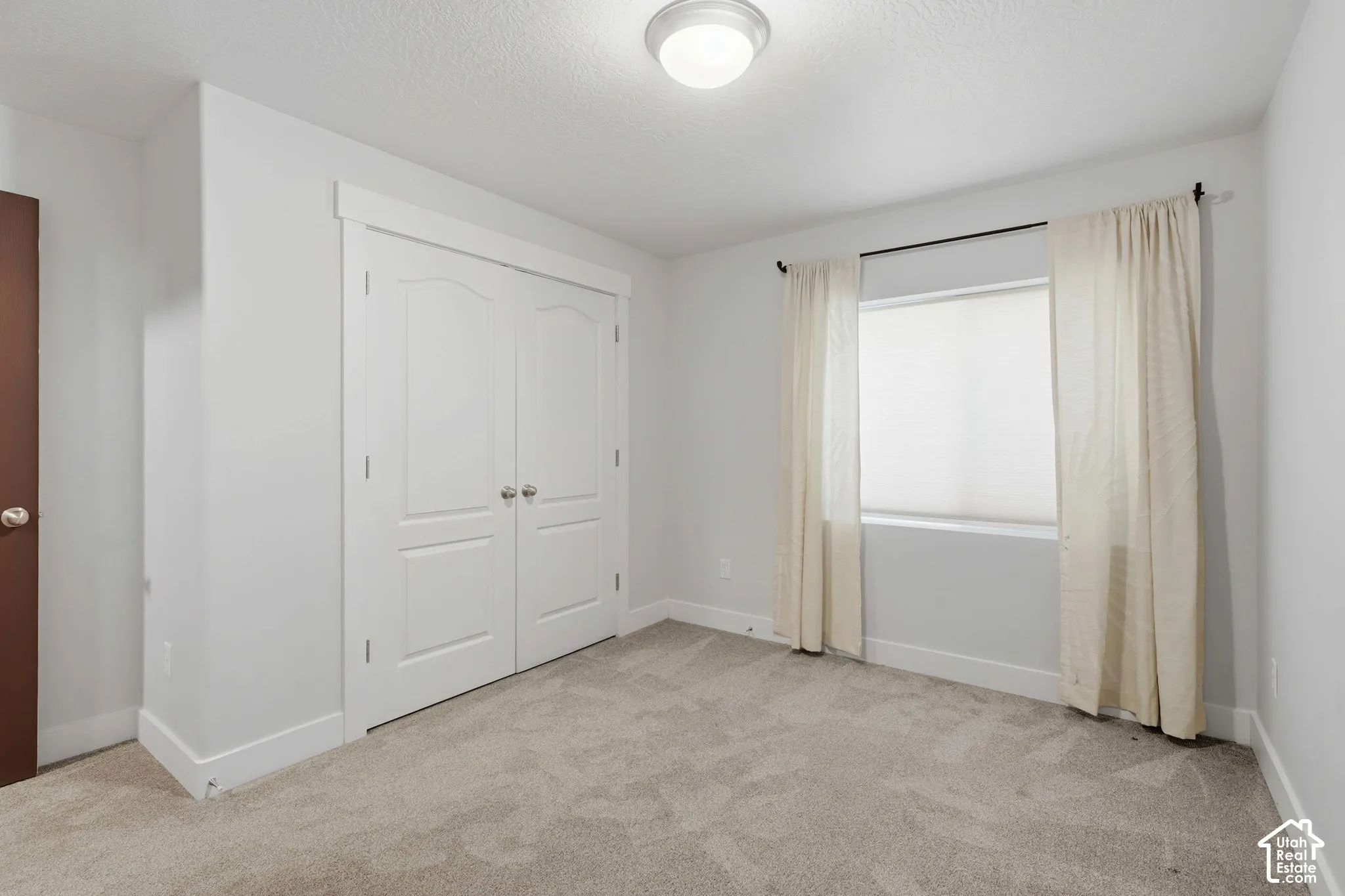 Neutral-toned carpeting, white walls, and a window with blinds and drapes