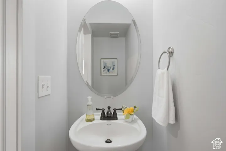 Pedestal sink with dark bronze-finish faucet, oval mirror, and chrome-finish towel ring