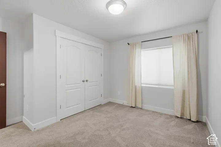 Neutral-toned carpeting, white walls, and a window with blinds and drapes