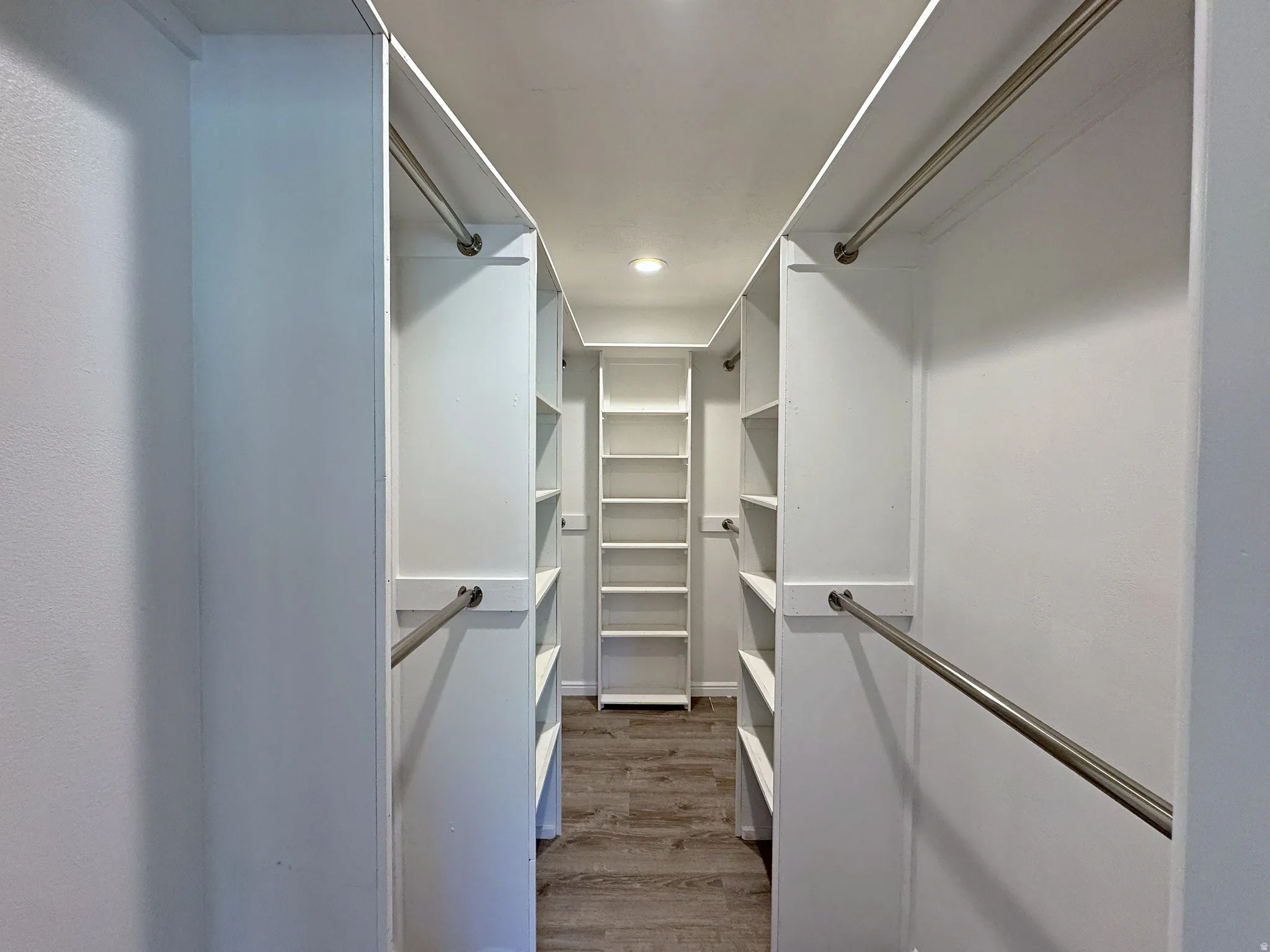 Walk-in closet featuring extensive built-in shelving, multiple hanging rods, recessed lighting, and wood-finish flooring