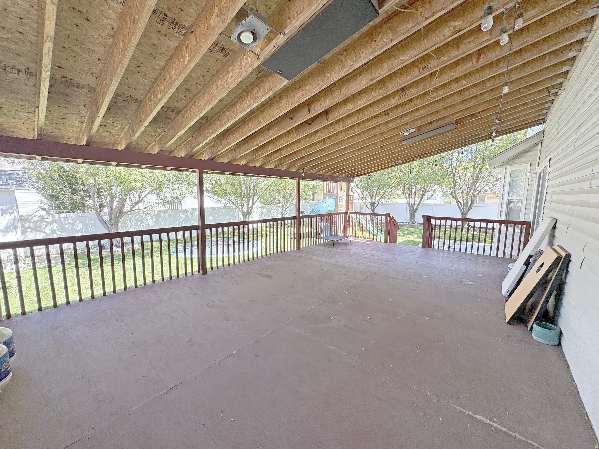 Expansive covered deck with wood-finish flooring, exposed wood beam ceiling, and a wooden railing overlooking a fenced yard