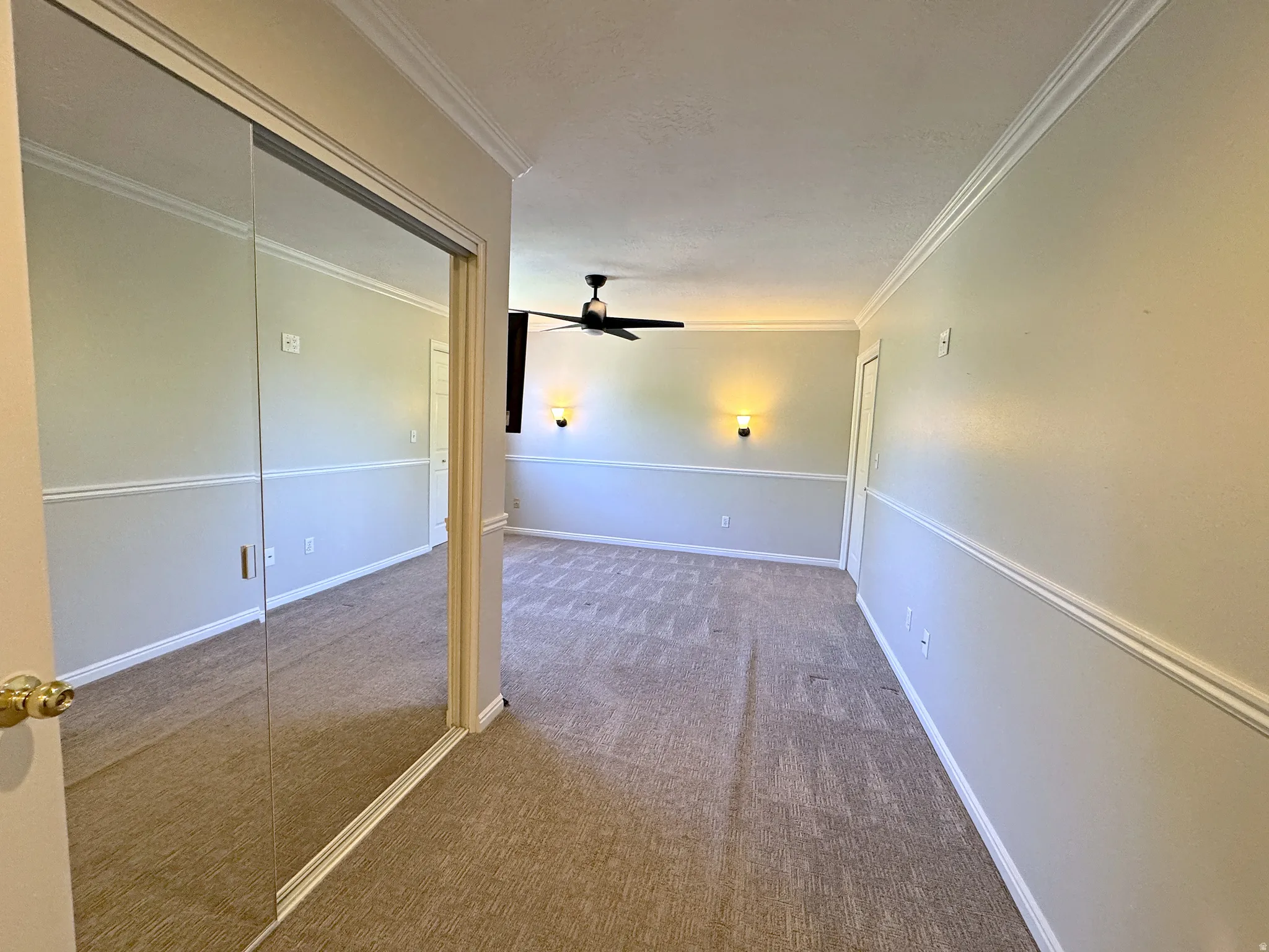 Mirrored sliding doors, crown molding, wall sconces, ceiling fan, and carpeted flooring