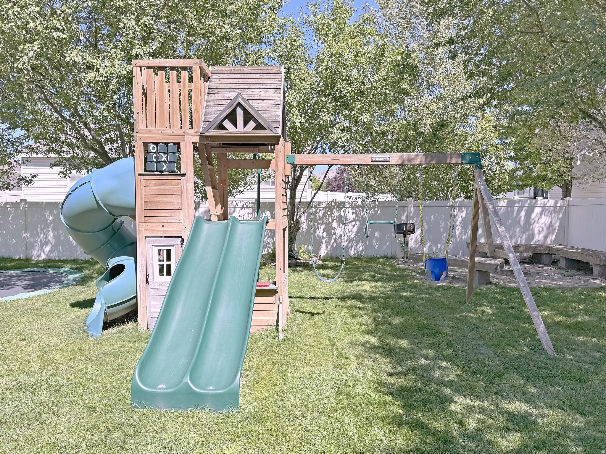 Expansive backyard with a manicured lawn, a wooden playset featuring two slides and a spiral slide, and a swing set