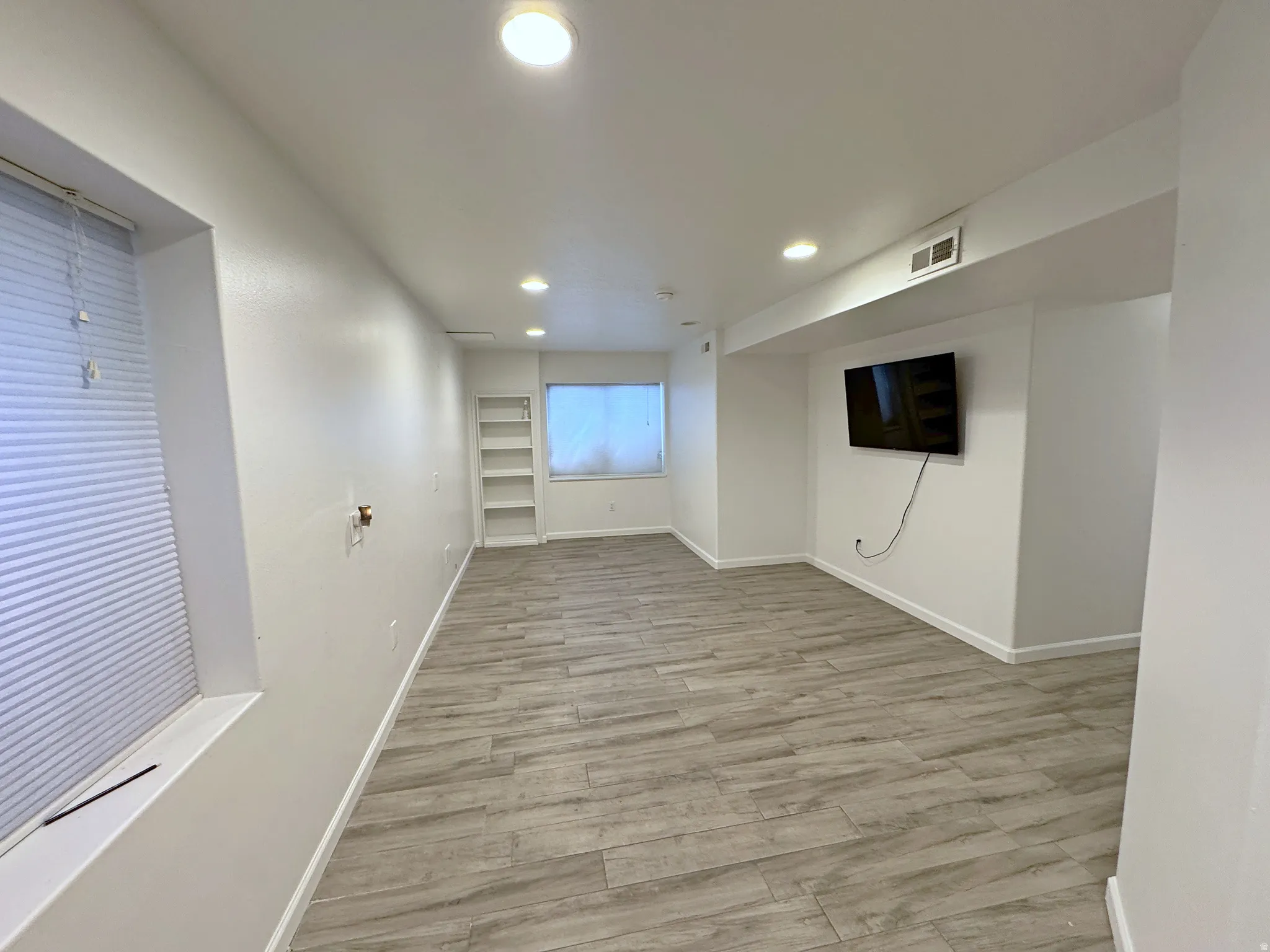 Recessed lighting illuminates the wood-finish flooring in this space featuring a built-in shelving unit and window treatments