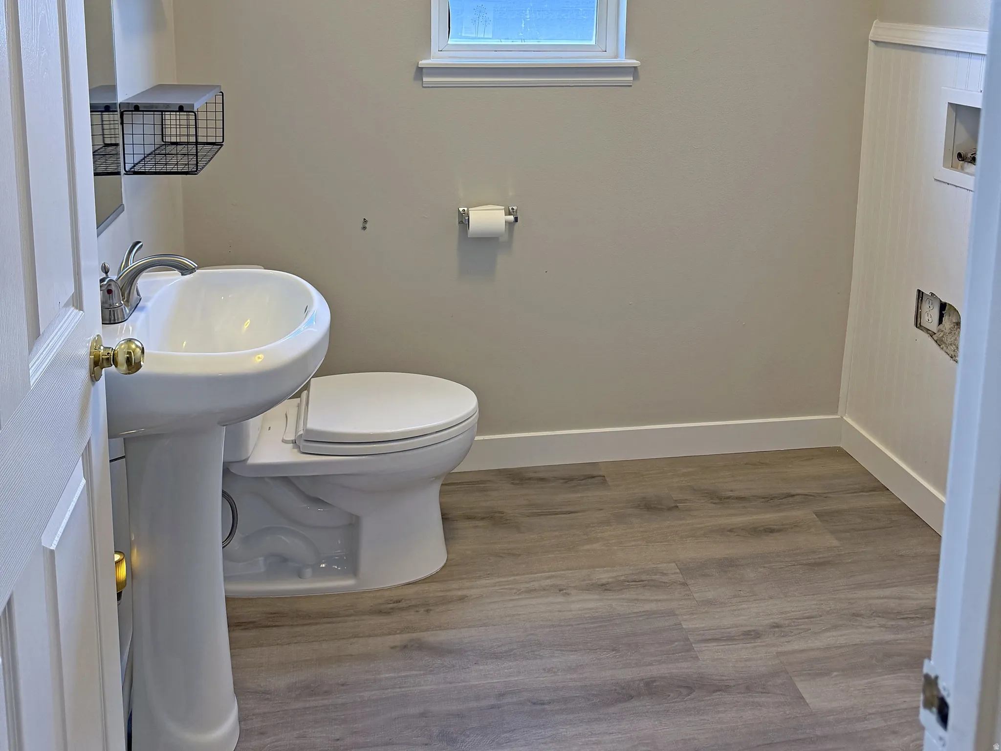 Pedestal sink, wall-mounted shelving, and wood-finish flooring