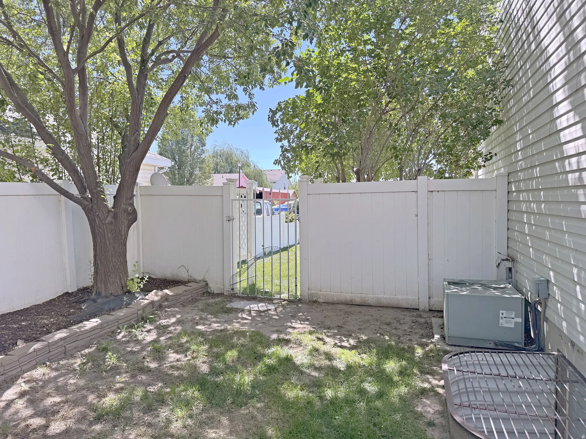 Private fenced yard with a mature tree, stone retaining wall, and side access gate
