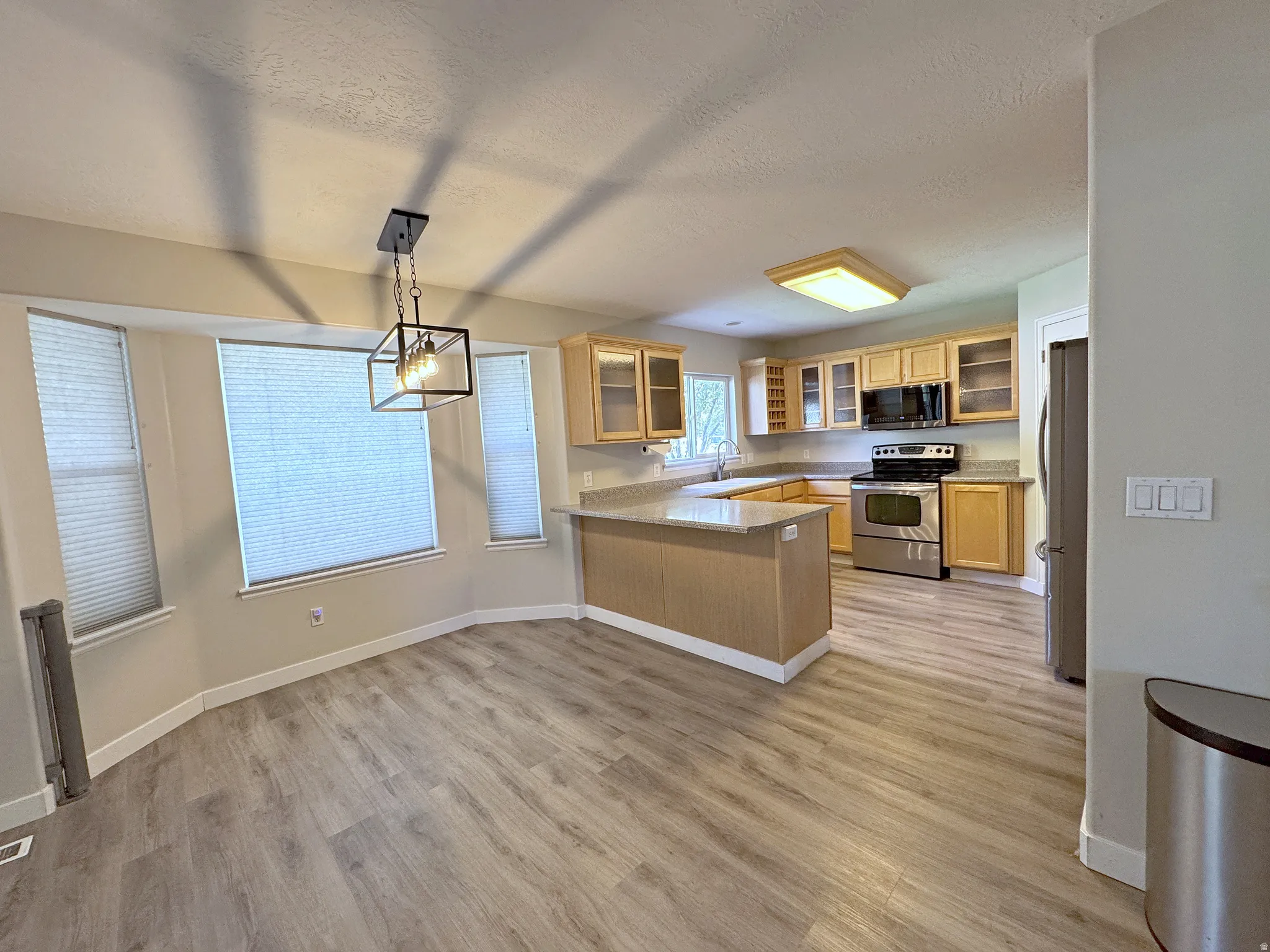 Kitchen with wood-finish flooring, light wood cabinetry, stainless steel appliances, and a peninsula with countertop seating