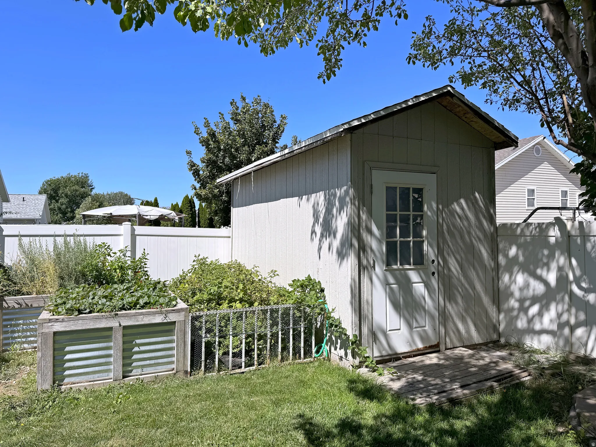 Storage shed with a single entry door, a white privacy fence, and raised garden beds