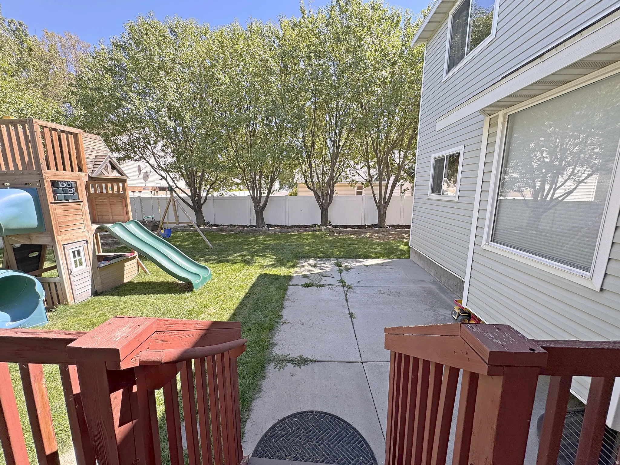 Expansive yard featuring a manicured lawn, mature trees, and a white privacy fence