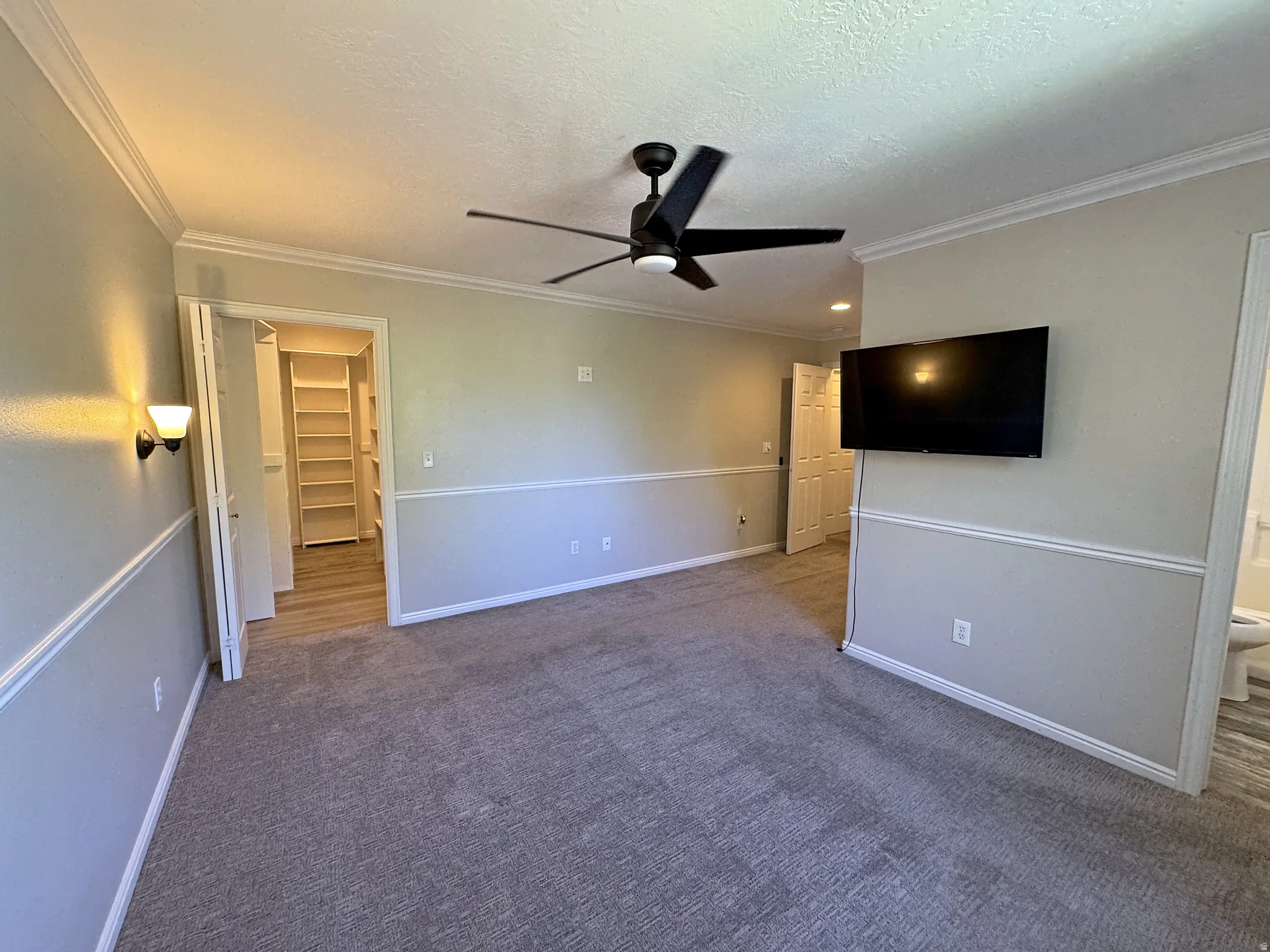 Ceiling fan with integrated lighting, wall sconce, crown molding, chair rail molding, and a built-in closet system