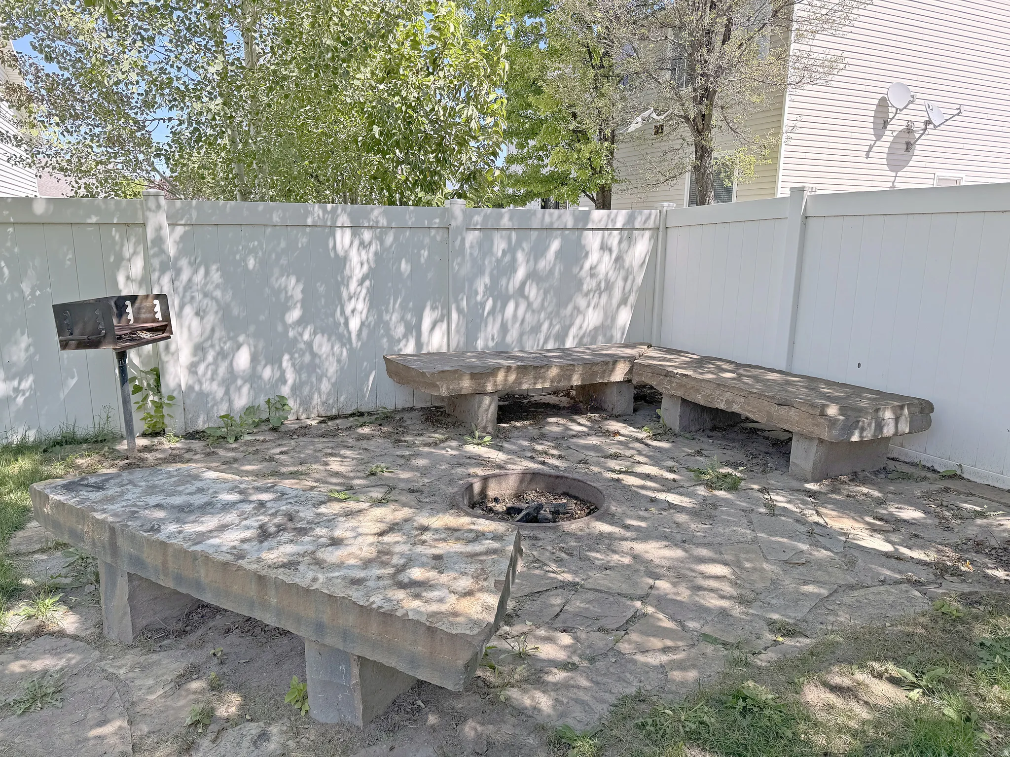 Private outdoor area featuring a vinyl fence, stone paver patio, built-in fire pit, three stone benches, and a permanent grill