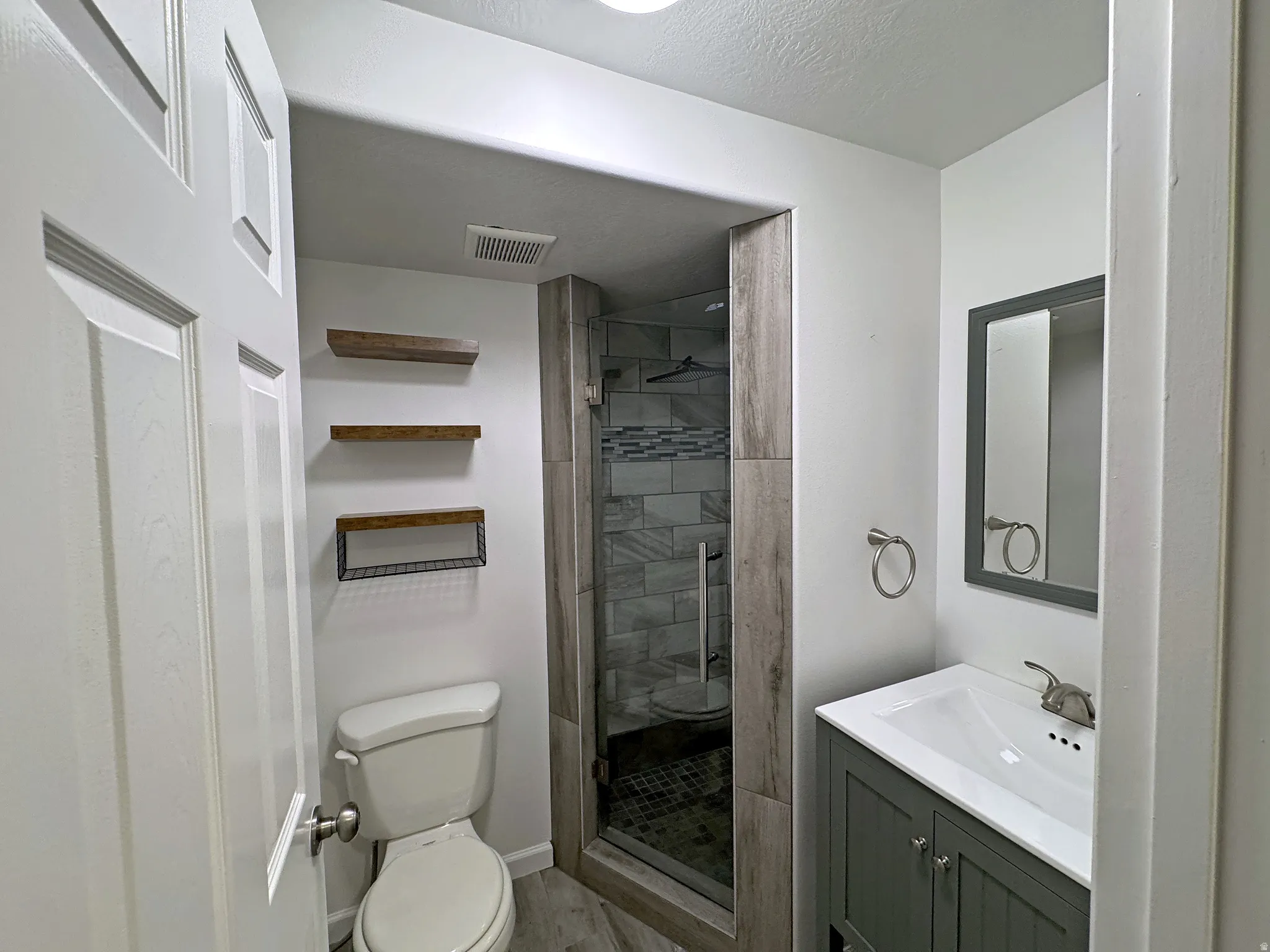 Full bathroom featuring a walk-in shower with tile surround, a single vanity with storage, and wood-finish flooring