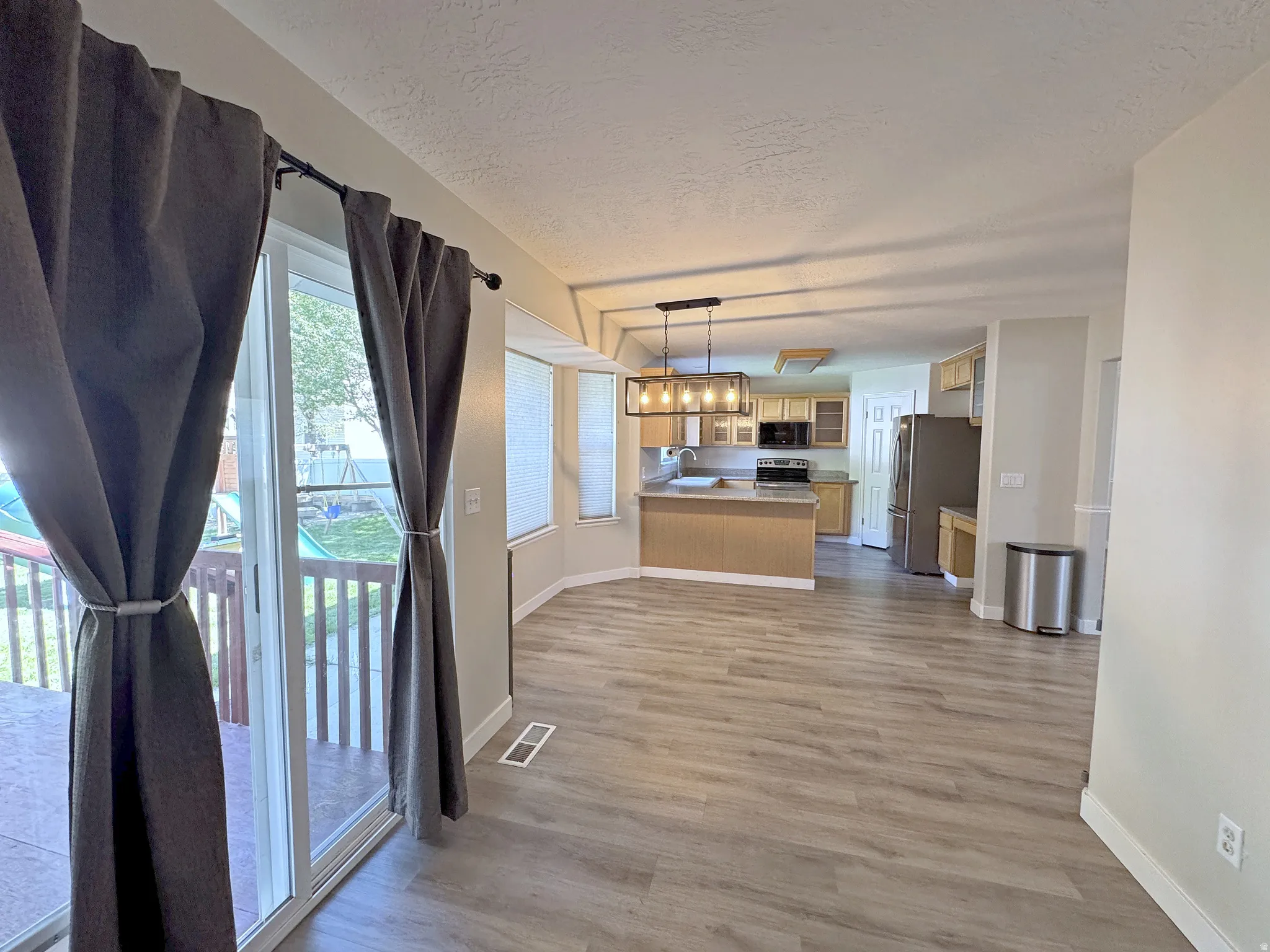 Open-concept living area with wood-finish flooring, a sliding glass door leading to an outdoor deck, and a kitchen featuring stainless steel appliances and pendant lighting